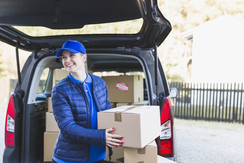 Professional mover carrying a packed moving box from a delivery vehicle during a residential relocation service.